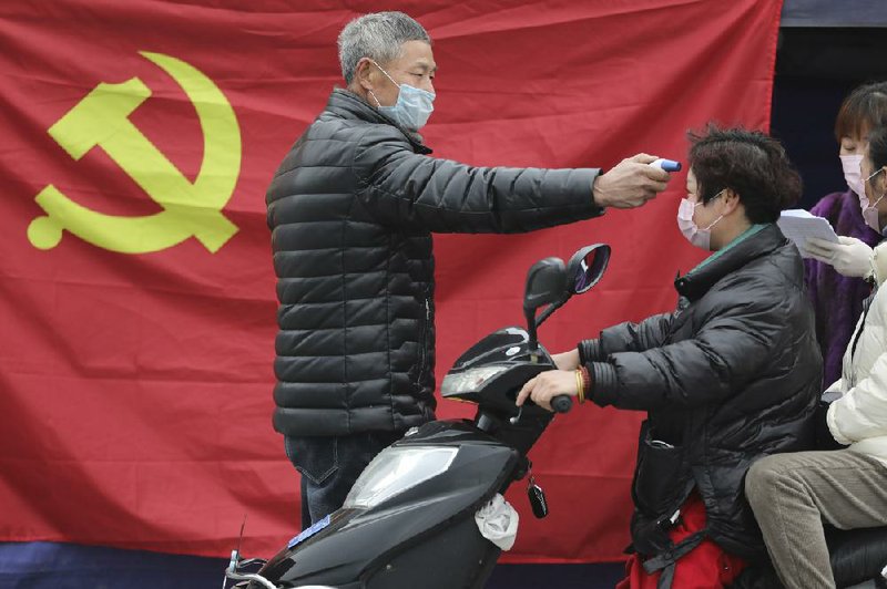 A volunteer takes the temperature of a scooter driver Monday at a roadside checkpoint in Hangzhou in eastern China’s Zhejiang province.