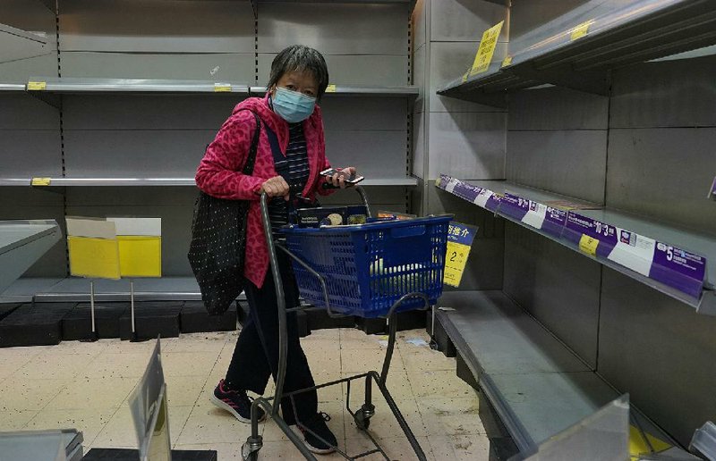 A woman wearing a protective mask moves past shelves emptied of facial tissue Thursday at a supermarket in Hong Kong. The coronavirus epidemic has much of China in a virtual standstill, and the effect is spilling across its borders. More photos at arkansasonline.com/27virus/.  