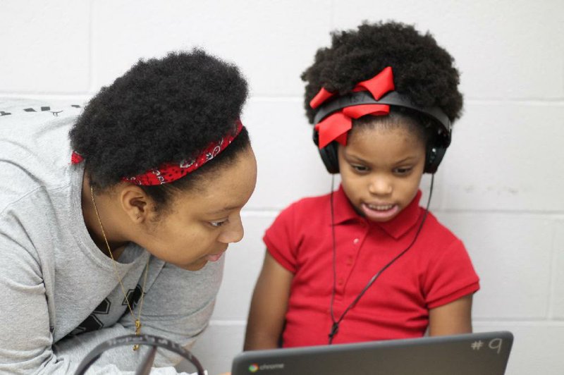 Zoey Cox, a first-grader at Romine Elementary School in Little Rock, receives help with a laptop from Tera Johnson, of Life Skills for Youth. Johnson, a former student of the after-school program, is currently one of its life skills coaches.  