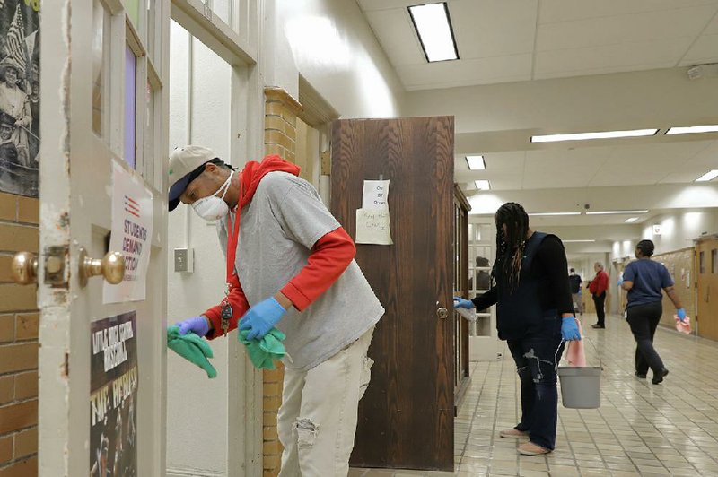 Carey James, part of a crew cleaning and disinfecting Little Rock Central High School, wipes down doorknobs and frames Monday. The Little Rock School District canceled classes Monday and today because of illnesses.  