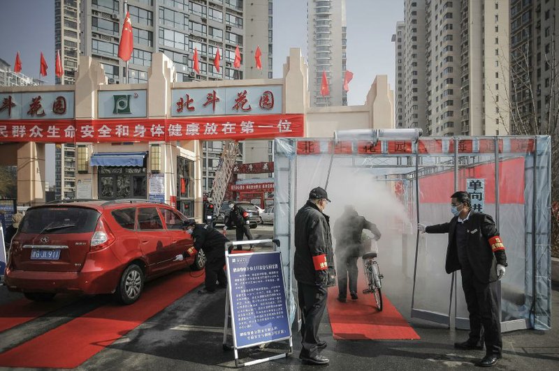 Security guards hold the curtain Tuesday for a cyclist to pass through a disinfectant spray as the cyclist returns home at a residential complex in northern China’s Tianjin Municipality. More photos at arkansasonline.com/213virus/
(AP/Chinatopix)