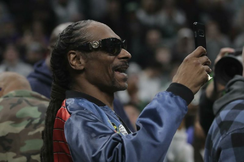 Rapper Snoop Dogg takes pictures prior to the first half of an NBA basketball game in Boston, Monday, Jan. 20, 2020. (AP Photo/Charles Krupa)