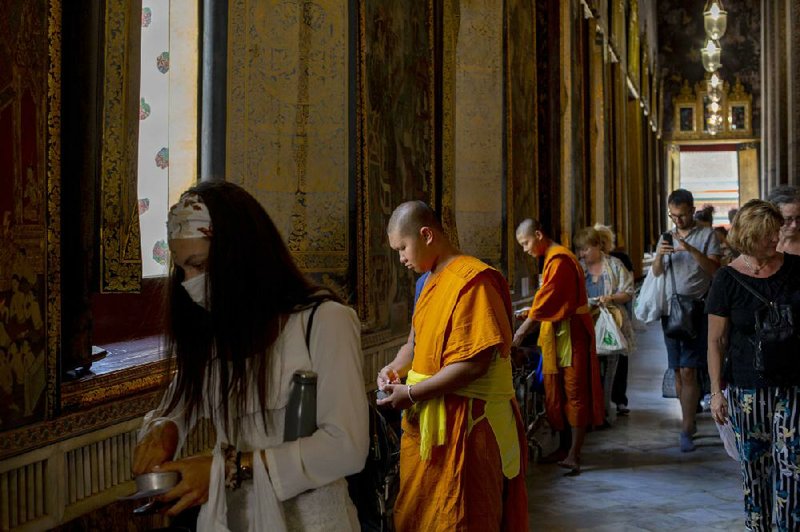Thai Buddhist monks and a tourist wearing a face mask drop coins into begging bowls at the Wat Pho temple last week in Bangkok.
(AP/Gemunu Amarasinghe)