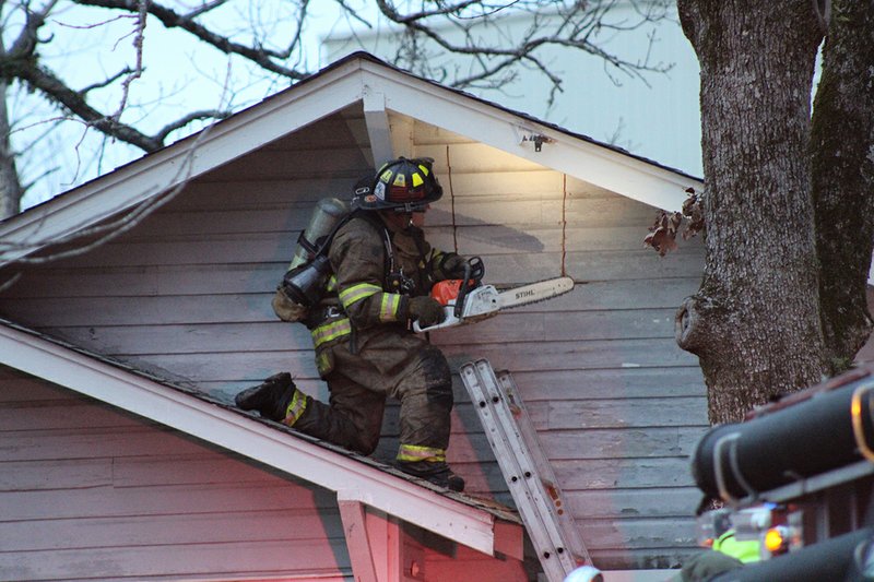 A firefighter uses a chain saw to cut into a residence at 2559 Spring St. on Wednesday. Cutter Morning Star Fire Department Capt. Joey Thompson said 10 firefighters from his department and three from Lake Hamilton Fire Department responded to the fire at 5:05 p.m. Thompson said that nobody was inside the building when it caught fire and that there were no injuries. Firefighter Matthew Walker said the cause of the fire is under investigation. - Photo by Tanner Newton of The Sentinel-Record