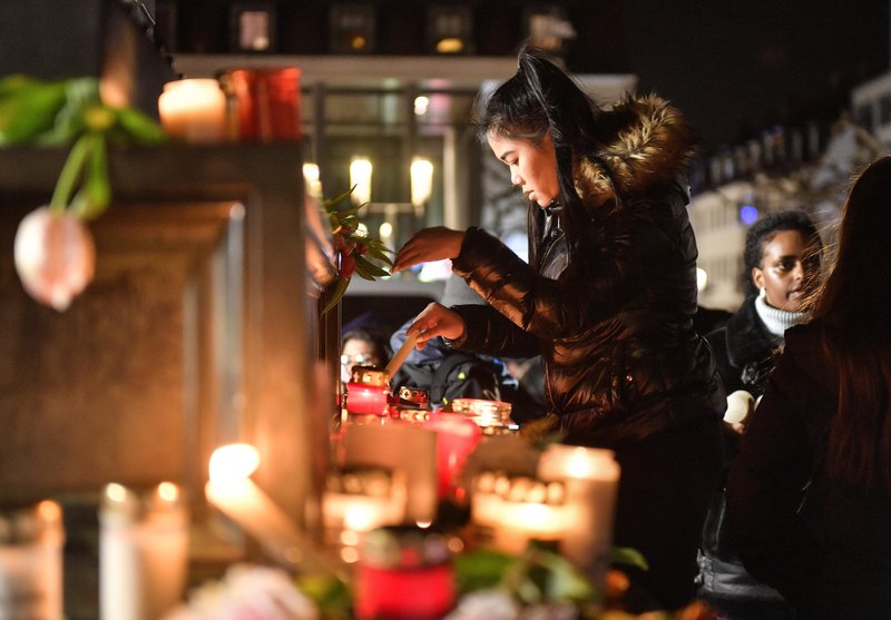 A woman lights a candle at a monument on the market place during a mourning for the victims of the shooting in Hanau, Germany, Thursday, Feb. 20, 2020. A 43-year-old German man shot and killed nine people at several locations in a Frankfurt suburb overnight in attacks that appear to have been motivated by far-right beliefs, officials said Thursday. (AP Photo/Martin Meissner)