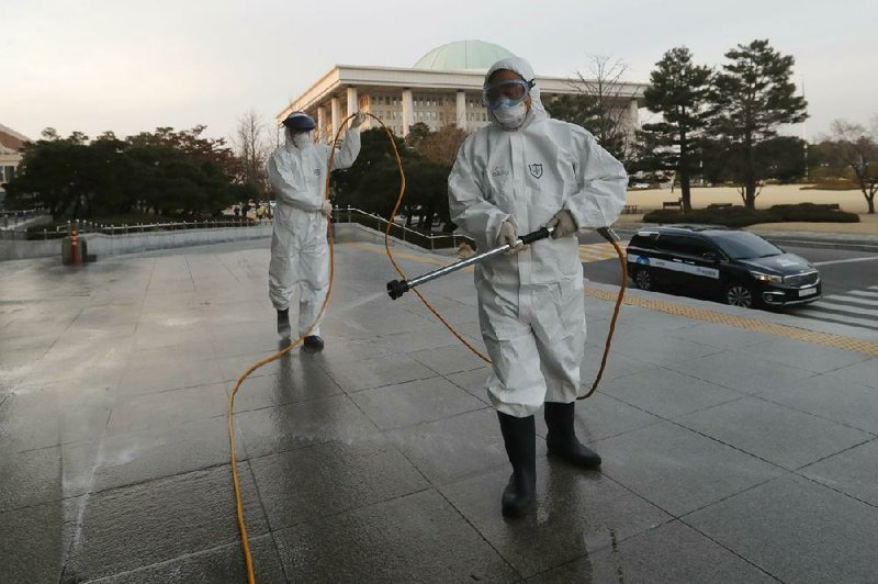 Workers in protective suits spray disinfectant Monday as a precaution against the coronavirus at the  National Assembly in Seoul, South Korea. More photos at arkansasonline.com/225virus/.
(AP/Ahn Young-Joon)