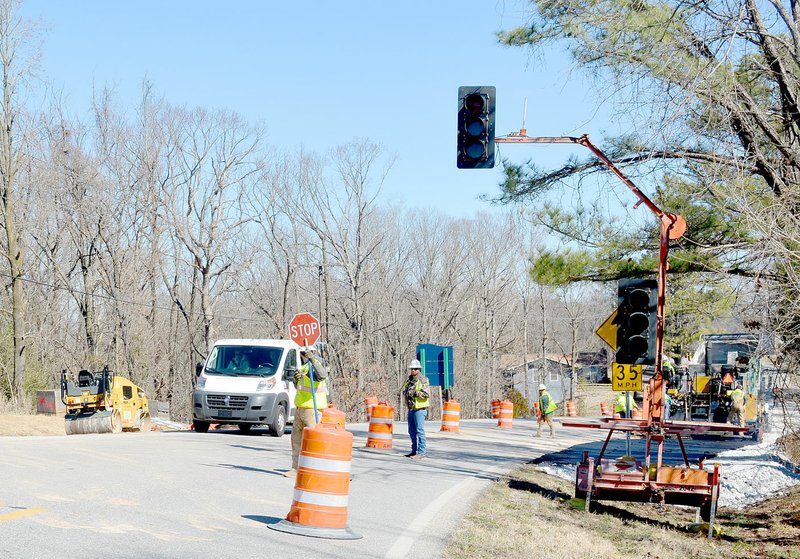 Keith Bryant/The Weekly Vista Workers direct traffic and lay asphalt for a temporary road alongside Arkansas Highway 340 in preparation for a trail tunnel to be installed at the site.