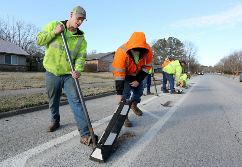 Dennis Vance (left) and Triston Phipps, both with Fayetteville's Transportation Division, remove bumpers Thursday with other department personnel on Rolling Hills Drive in Fayetteville. City crews anticipate working through Saturday to remove the bumpers and replace them with flat reflectors. Go to nwaonline.com/200228Daily/ and nwadg.com/photos for a photo gallery. (NWA Democrat-Gazette/David Gottschalk)