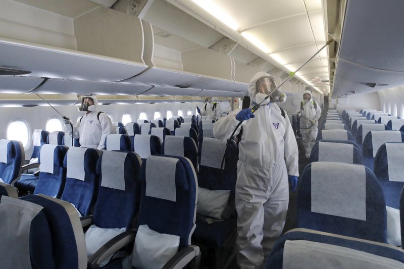 Workers wearing protective gears spray disinfectant inside a plane for New York as a precaution against the new coronavirus at Incheon International Airport in Incheon, South Korea, Wednesday, March 4, 2020. The coronavirus epidemic shifted increasingly westward toward the Middle East, Europe and the United States on Tuesday, with governments taking emergency steps to ease shortages of masks and other supplies for front-line doctors and nurses. (Suh Myoung-geon/Yonhap via AP)

