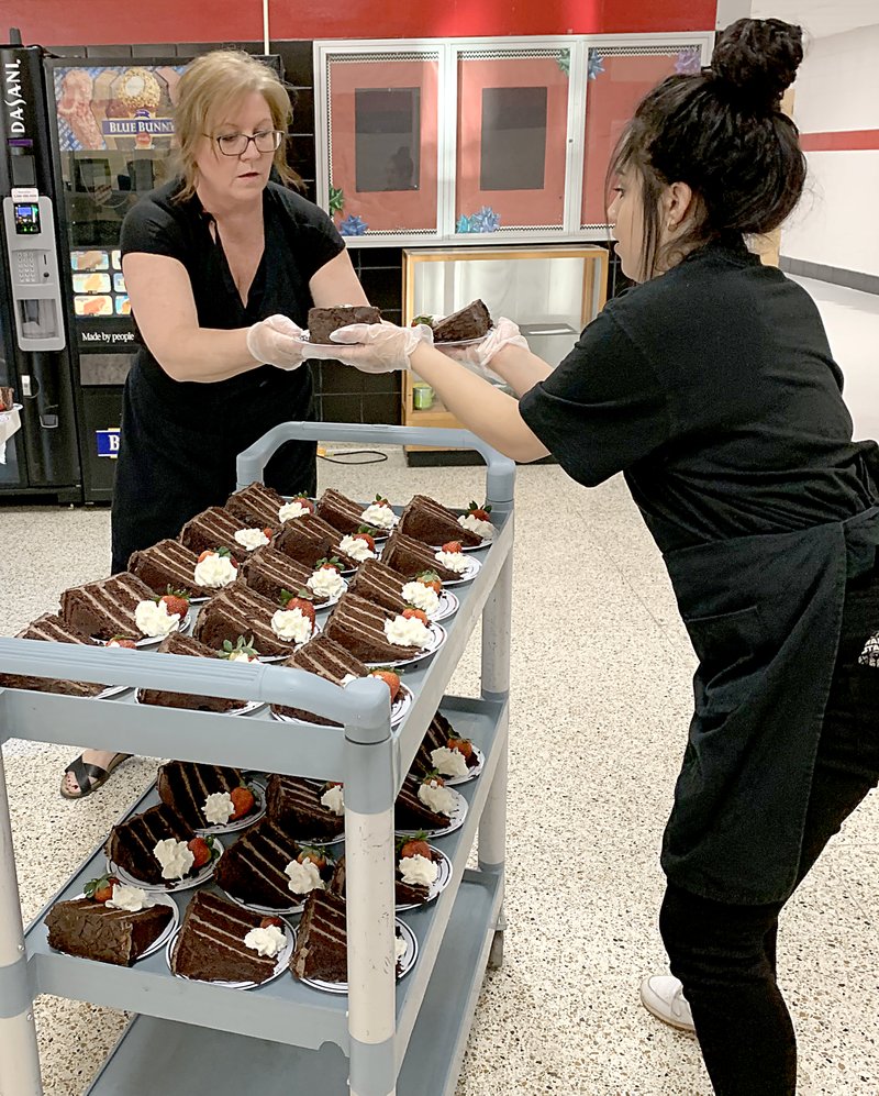 Sally Carroll/McDonald County Press Melody Poland hands Veronica Avalos dessert plates of chocolate cake as a crew readies the food at the Heart of Education Banquet Saturday night.