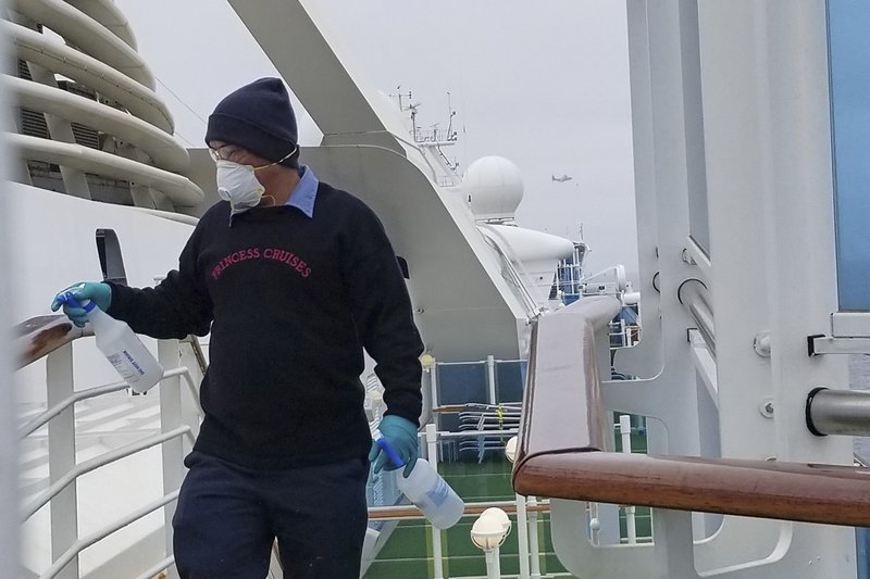 In this photo provided by Michele Smith, a cruise ship worker cleans a railing on the Grand Princess Thursday, March 5, 2020, off the California coast. Scrambling to keep the coronavirus at bay, officials ordered a cruise ship with about 3,500 people aboard to stay back from the California coast Thursday until passengers and crew can be tested, after a traveler from its previous voyage died of the disease and at least two others became infected.  (Michele Smith via AP)