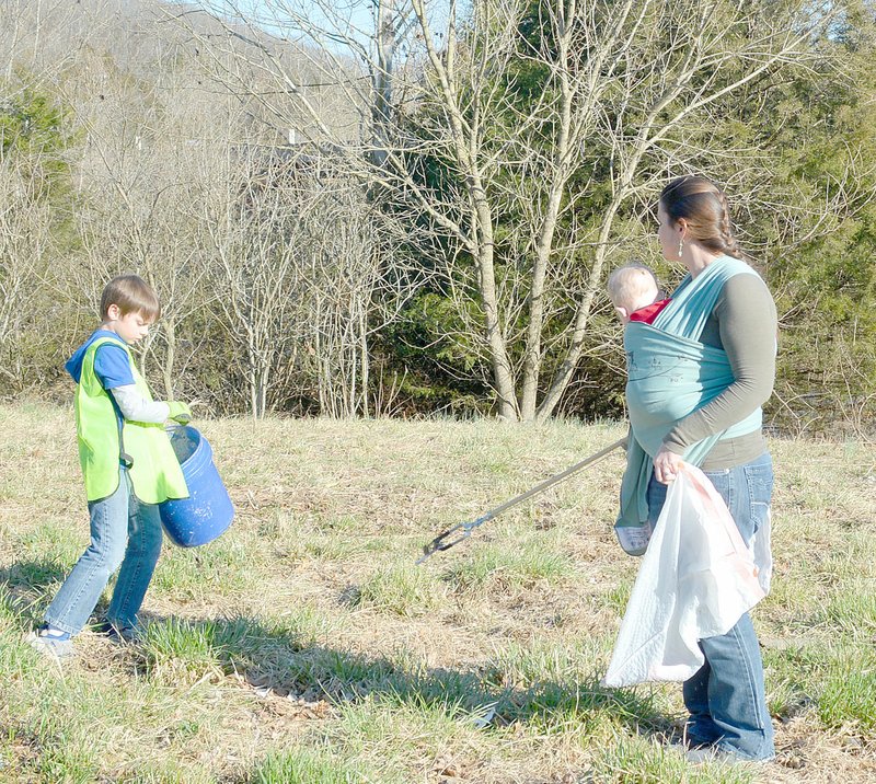 Keith Bryant/The Weekly Vista Nathan Sanders, 8, works with Rebecca Fraley while she carries seven-month-old Alexander Fraley and picks up trash alongside Mercy Way.