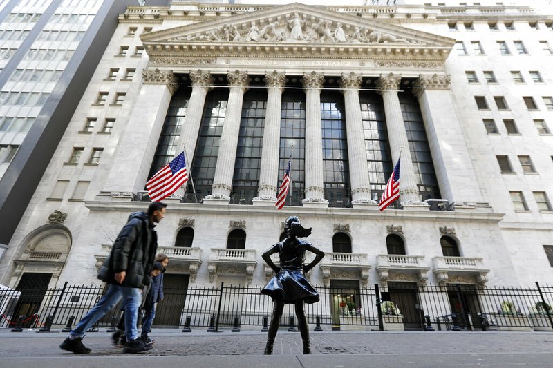 People pass the New York Stock Exchange, and the Fearless Girl statue, on Sunday, March 15, 2020.