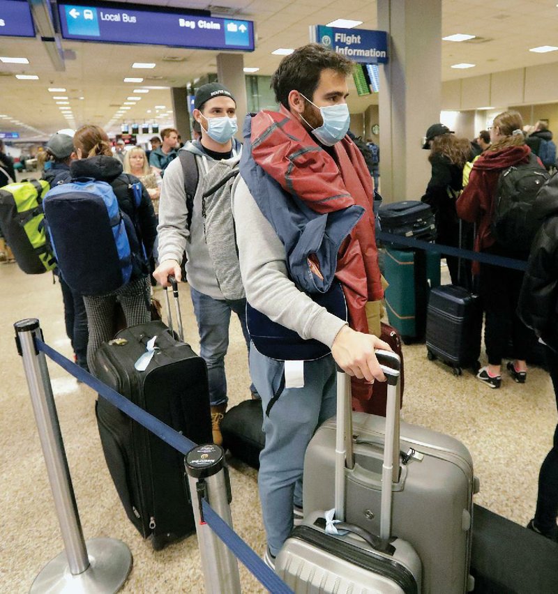 Masked travelers stand in line Sunday before getting to the ticket counter at the Salt Lake City In- ternational Airport. Health screenings at airports contributed to crowded terminals, long lines and hours-long delays over the weekend across the United States. More photos available at arkansa- sonline.com/316covid/. 
(AP/Rick Bowmer) 
