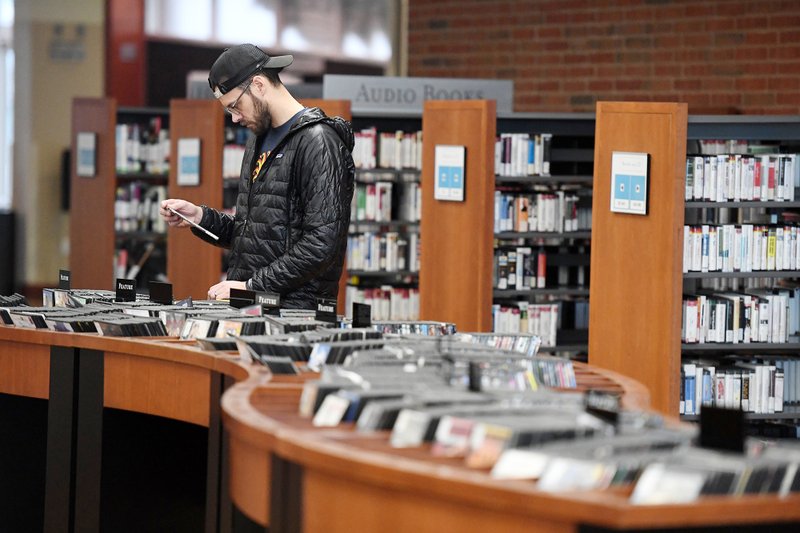 Ryan Masten of Fayetteville looks through DVDs Monday at the Fayetteville Public Library. Masten, a school teacher, was preparing to spend time at home with his family since there is no school. The Library closed at noon Monday with plans to reopen after March 29. Libraries across Northwest Arkansas have closed to help stop the spread of the coronavirus covid 19. For more information see www.faylib.org. Go to nwaonline.com/200317Daily/ for more images. (NWA Democrat-Gazette/J.T. Wampler)