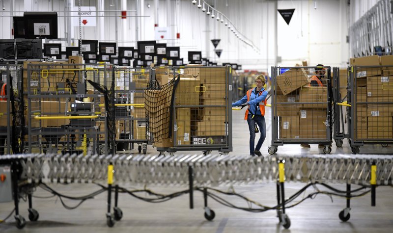 FILE - In this Friday, March 23, 2018, file photo, associates move bins filled with products at the loading dock of Amazon's then-new fulfillment center in Livonia, Mich. On Monday, March 16, 2020, Amazon said that it needs to hire 100,000 people across the U.S. to keep up with a crush of orders as the coronavirus spreads and keeps more people at home, shopping online. (Todd McInturf/Detroit News via AP, File)