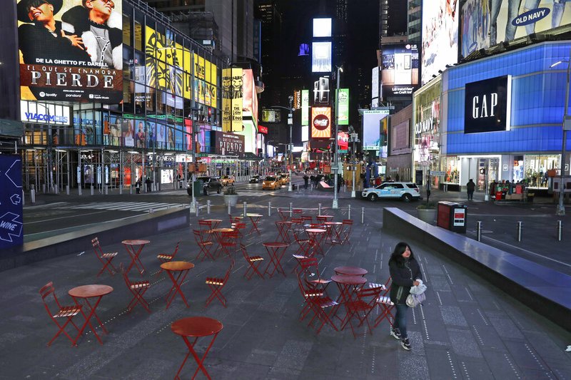 A woman walks through a lightly trafficked Times Square in New York, Monday, March 16, 2020. Bars and restaurants will become takeout-only and businesses from movie theaters and casinos to gyms and beyond will be shuttered Monday night throughout New York, New Jersey and Connecticut because of the coronavirus, the states' governors said. (AP Photo/Seth Wenig)