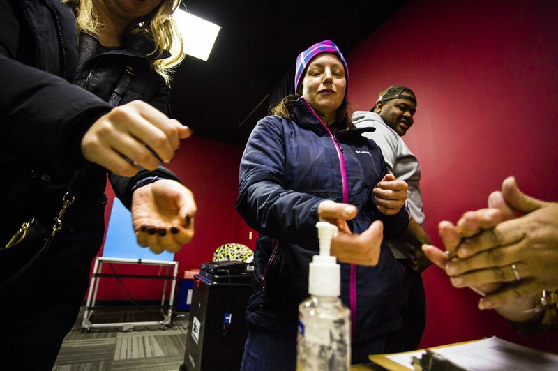 Sharon Trask and other voters use hand sanitizer as they stand in line to vote at Lincoln Lodge Polling station, 1st ward, Tuesday, March 17 2020 in Chicago. Voters across the state are getting the chance to decide competitive primary races for the U.S. House and the Illinois Supreme Court, with concerns about the coronavirus looming large. Election officials have been promoting voting early and casting ballots by mail in an attempt to control crowds and curb the spread. The vast majority of people recover from the new coronavirus. According to the World Health Organization, most people recover in about two to six weeks, depending on the severity of the illness. (James Foster/Chicago Sun-Times via AP)