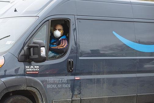 A driver wears a protective mask last week while traveling in an Amazon.com Inc. delivery truck in New Rochelle, N.Y. Amazon Inc. is handling a surge in demand for online orders from customers avoiding stores during the coronavirus pandemic. (Bloomberg News/Angus Mordant) 