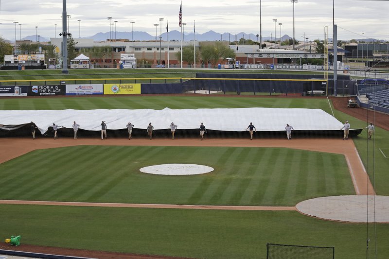 Grounds crew members pull a tarp toward the infield to cover it in anticipation of coming rain after a spring training baseball game between the Los Angeles Angels and the Seattle Mariners Tuesday, March 10, 2020, in Peoria, Ariz. (AP Photo/Elaine Thompson)