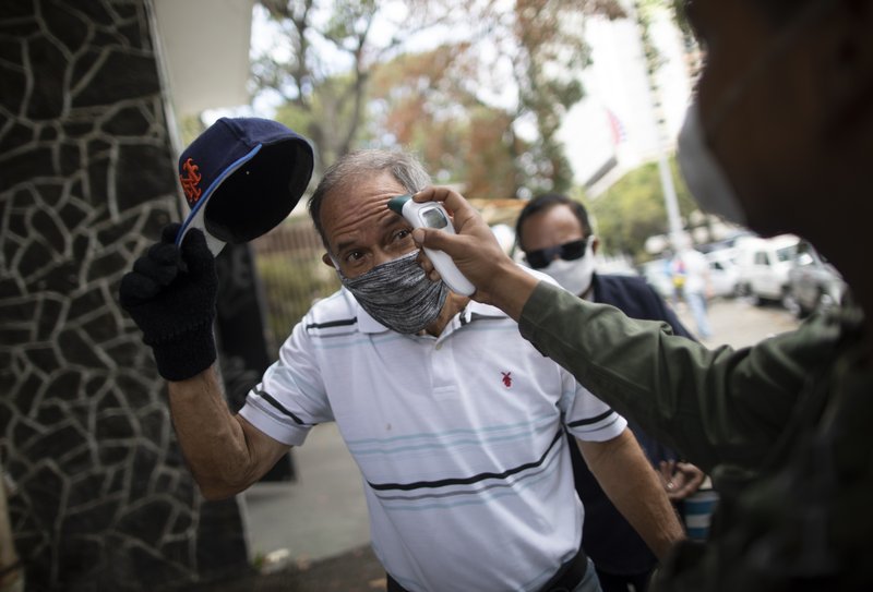 A man removes his cap as a soldier takes his temperature outside a food market as a preventative measure against the spread of the coronavirus in Caracas, Venezuela, Thursday, March 19, 2020. To enter the market, people are required to get their temperature taken and disinfect their hands. (AP Photo/Ariana Cubillos)