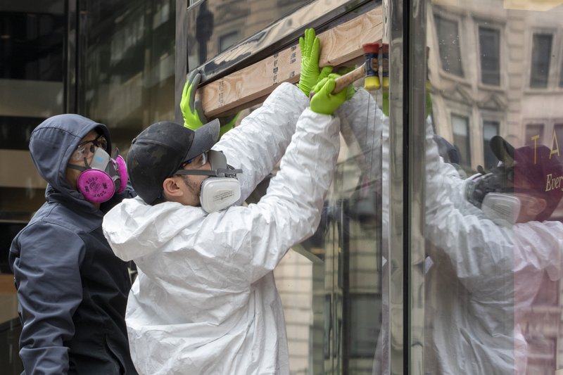 Carpenters wear protective gear as they board up the closed Sephora store on 34th St., Friday, March 20, 2020, in New York.  (AP Photo/Mary Altaffer)
