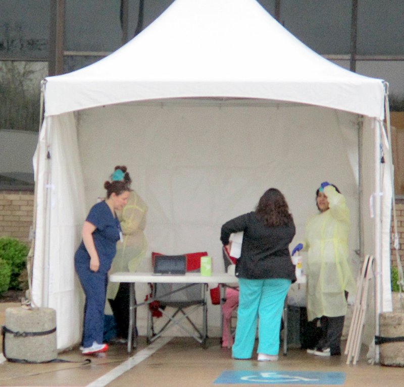 Marc Hayot/Siloam Sunday Medical workers set up a tent around the Community Clinic covid-19 evaluation and testing site in Siloam Springs during rainy weather on Thursday. Community Clinic opened four covid-19 testing sites in Northwest Arkansas, including the location outside the Siloam Springs clinic at 500 S. Mt. Olive St. Patients with symptoms of the virus are asked to call 1-855-438-2280 for screening and to set up an appointment at an evaluation site. Northwest Health and Community Physicians Group clinics also provide evaluation and testing according to CDC guidelines, and patients with symptoms are asked to call their health care provider before going to a clinic.