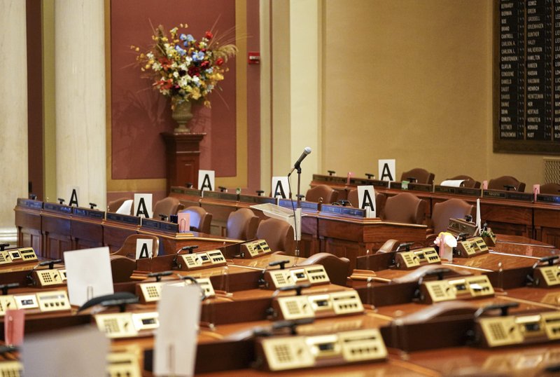 FILE - In this Wednesday, March 18, 2020 file photo, the House chamber at the state Capitol is empty in St. Paul, Minn., with some desks marked with an "A" - those desks may be occupied when lawmakers return to maintain "social distancing" because of the COVID-19 coronavirus.(Glen Stubbe/Star Tribune via AP)