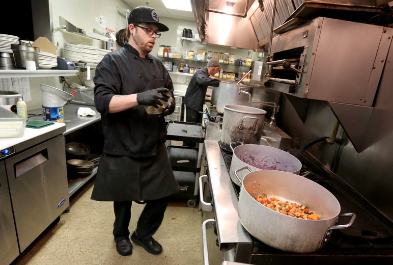 Corey McCain, executive chef at Bordinos, prepares a free family meal for laid-off employees and family members to pick up Thursday at the restaurant on Dickson Street in Fayetteville. Restaurants and bars in the city of Fayetteville are making adjustments because of the spread of covid-19. (NWA Democrat-Gazette/David Gottschalk)