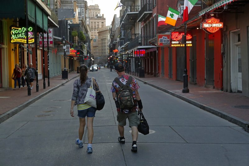 People walk down a nearly empty Bourbon Street in the French Quarter of New Orleans on Thursday, March 19, 2020. The street is usually bustling with tourists.