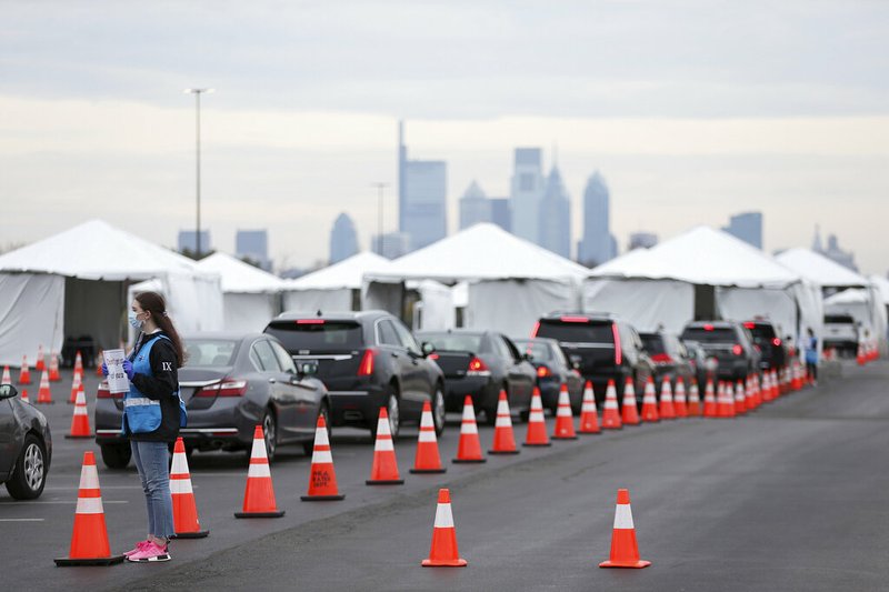 FILE - In this Friday, March 20, 2020 photo, a Philadelphia Medical Reserve Corps volunteer, left, directs cars at the city's covid-19 coronavirus testing site in South Philadelphia, the first city-run drive-through location for coronavirus testing. 
