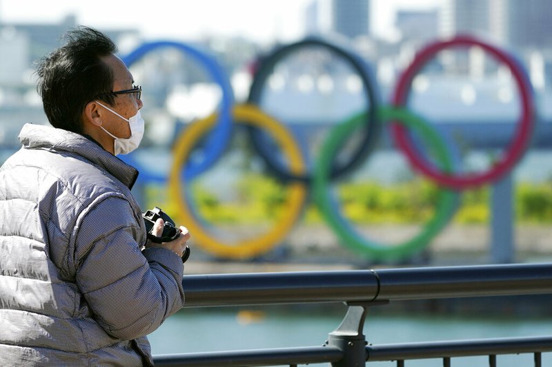 A visitor wearing a face mask stands near the Olympic rings at Tokyo's Odaiba district Tuesday, March 24, 2020. The Tokyo Olympics are probably going to happen, but almost surely in 2021 rather than in four months as planned. (AP Photo/Eugene Hoshiko)
