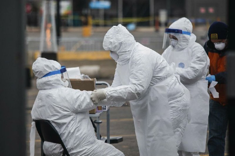 Medical workers help each other with their suits on Sunday at a drive-thru testing site in the parking lot of a Walmart store in Northlake, Ill. (Chicago Sun-Times/Pat Nabong) 