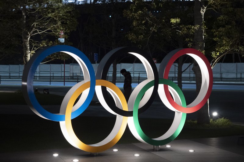 A man is seen through the Olympic rings in front of the New National Stadium in Tokyo, Tuesday, March 24, 2020. IOC President Thomas Bach has agreed &quot;100%&quot; to a proposal of postponing the Tokyo Olympics for about one year until 2021 because of the coronavirus outbreak, Japanese Prime Minister Shinzo Abe said Tuesday. (AP Photo/Jae C. Hong)