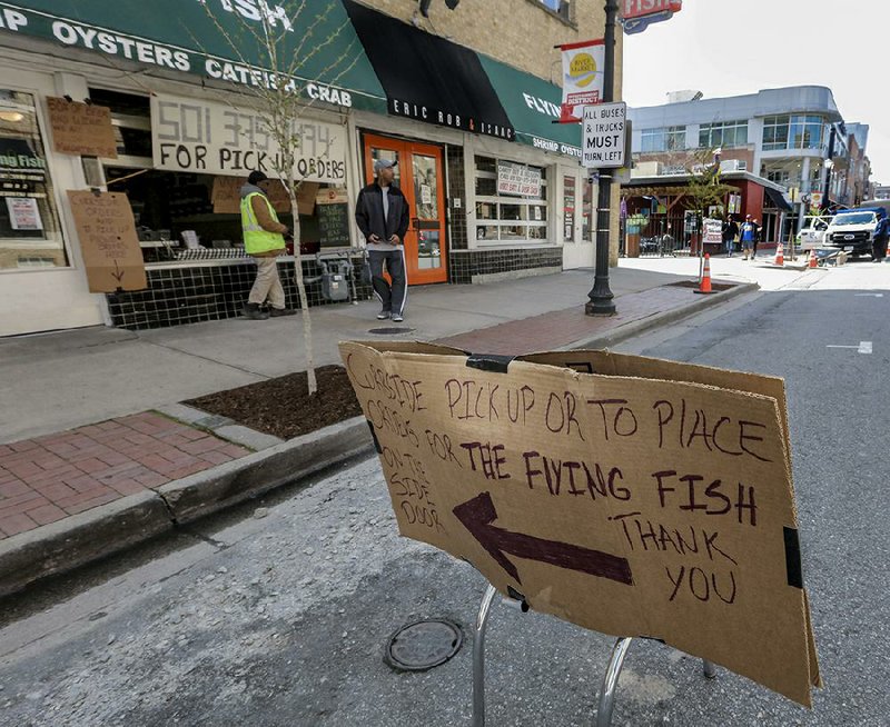 Mike Mays waits  for his  lunch Wednesday near makeshift signs showing customers where to pick up their food outside the Flying Fish restaurant in downtown Little Rock. Many Little Rock restaurants are limiting service to curbside or carryout because of coronavirus restrictions. 
Arkansas Democrat-Gazette/John Sykes Jr.)