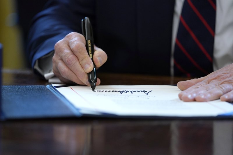 President Donald Trump signs the coronavirus stimulus relief package in the Oval Office at the White House on Friday, March 27, in Washington. - AP Photo/Evan Vucci