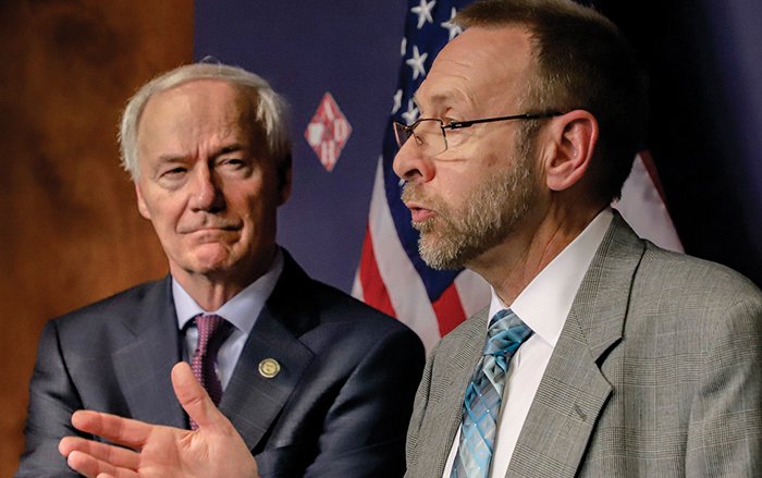 Gov. Asa Hutchinson (left) listens to Health Department Secretary Dr. Nate Smith in Little Rock on Tuesday. The governor said Tuesday that President Donald Trump was “speaking in a hopeful way” about reopening the country by Easter.
