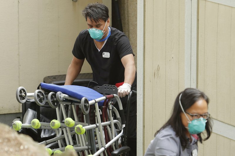 Workers at Life Care Center in Kirkland, Wash., near Seattle, wear masks as they move walkers and other mobility aids that have been cleaned out of the center and into a portable storage unit, in this March 17, 2020, file photo near Seattle.