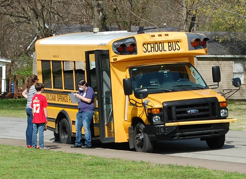 Janelle Jessen/Siloam Sunday School employee Ashley Shoptaw helps pass out food from a school bus near Bob Henry Park on Thursday. The Siloam Springs School District is expanding its meal program starting Monday to deliver lunches and breakfasts on regular bus routes between 10 and 11:15 a.m.