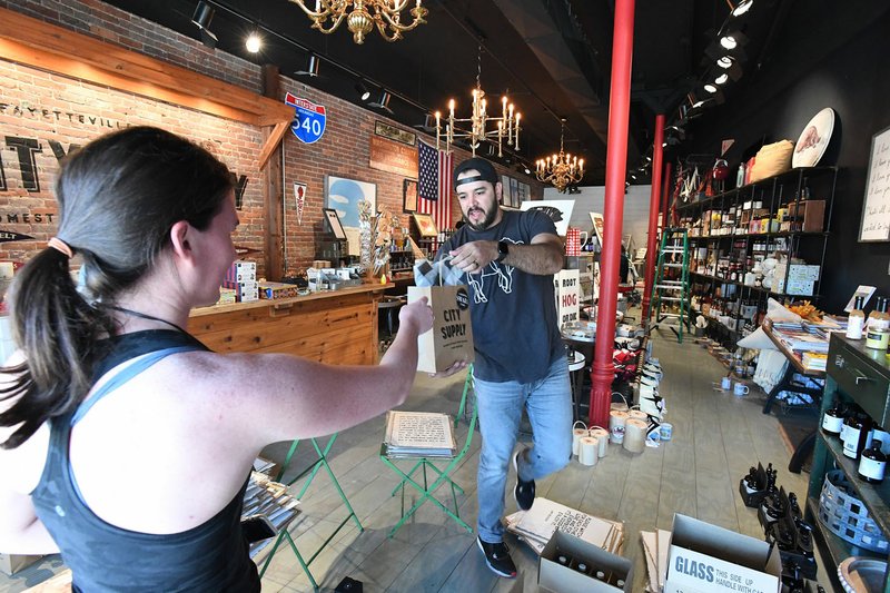 Annie Montague of Fayetteville picks up an order for a friend from owner Chase Norman Wednesday at City Supply in Fayetteville. The business is closed to walk-in customers but is filling orders for customers to pick up. Financial officers in Northwest Arkansas cities and counties say there are too many variables at stake to accurately know what the impact to regional sales tax could be in the midst of the covid-19 pandemic. Visit nwaonline.com/200329Daily/ for more images. (NWA Democrat-Gazette/J.T. Wampler)