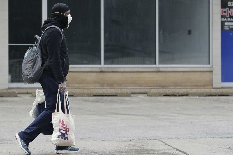 A pedestrian carries shopping bags Saturday on a street in Chicago. Restrictions ordered Friday by Gov. J.B. Pritzker are taking a toll on workers and especially poor people. More photos at arkansasonline.com/329heartland/.
(AP/Nam Y. Huh)