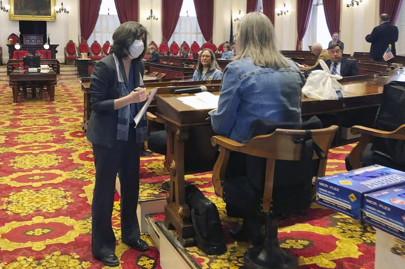 FILE - In this March 25, 2020 file photo, Vermont House Speaker Mitzi Johnson, left, wears a mask while talking to a lawmaker in the Vermont house chamber at the Statehouse in Montpelier, Vt. In state capitols across the U.S., lawmakers have ditched decorum and sidestepped traditional public meeting requirements in a rush to pass legislation funding the fight against the coronavirus and aiding residents affected by the widespread shut down of commerce. (AP Photo/Wilson Ring, File)