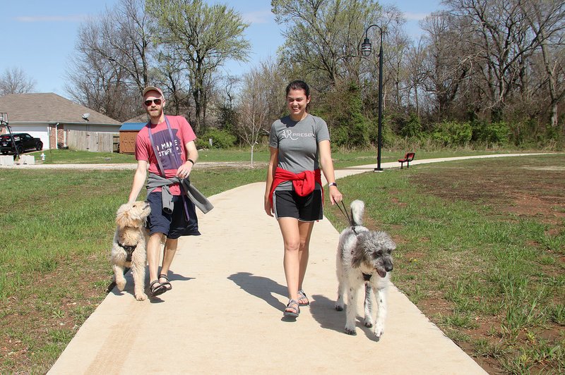 LYNN KUTTER ENTERPRISE-LEADER Jacob and Brianne Christiansen, of Farmington, walk their dogs, Cricket and Calvin, last week at Creekside Park in Farmington. Both are youth pastors with First United Presbyterian Church in Fayetteville. They are working from home now because of covid-19 concerns and figuring out how to minister to their youth through other ways. Exercise is one recommendation given by counselors and therapists as a way to deal with anxiety or stress because of the coronavirus.