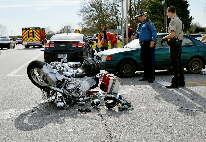 TIMES photograph by Annette Beard State Trooper Mike Morgan looked over the Honda motorcycle involved in a two-vehicle collision on U.S. Highway 62 at the intersection with Ark. Highway 72 Saturday evening. The driver of the motorcycle was killed; the passenger was taken by ambulance to a landing zone to meet the helicopter ambulance and was taken to Washington Regional Memorial Hospital. She was transferred to a hospital in Springfield, Mo.