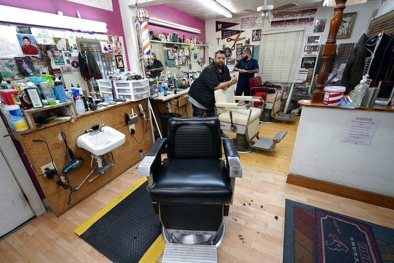In this Friday, March 20, 2020 file photo, Carlos Vasquez, left, and his nephew, R.J. Vasquez, wait for customers at their family's barber shop in Houston. They estimate they have lost nearly half of their business due to the COVID-19 coronavirus. (AP Photo/David J. Phillip)