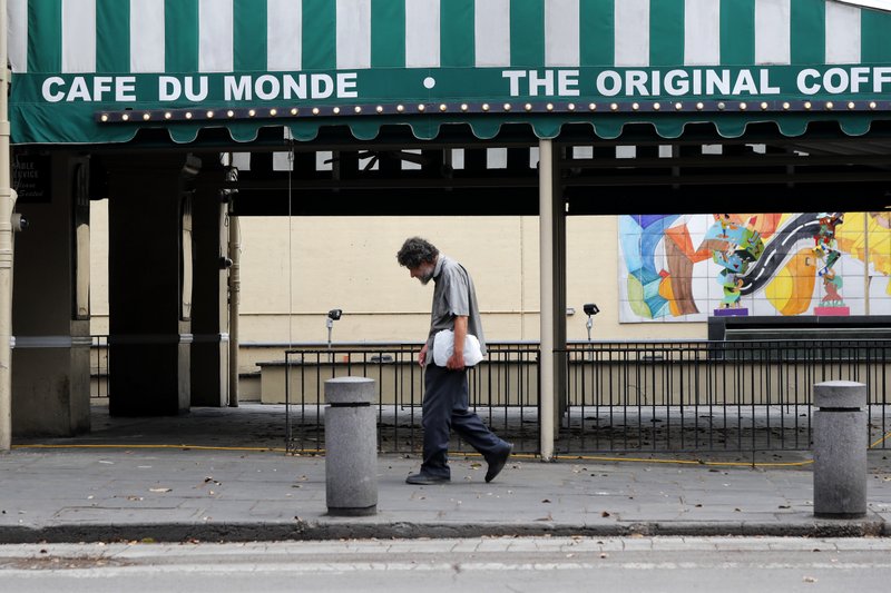 FILE - In this Friday, March 27, 2020 file photo, a man walks past the closed Cafe Du Monde restaurant in the French Quarter of New Orleans. It's normally bustling with tourists, but now nearly deserted due to the COVID-19 coronavirus pandemic. While rich in history and culture, New Orleans is economically poor, and many here are not necessarily well-positioned to weather this latest storm. (AP Photo/Gerald Herbert)