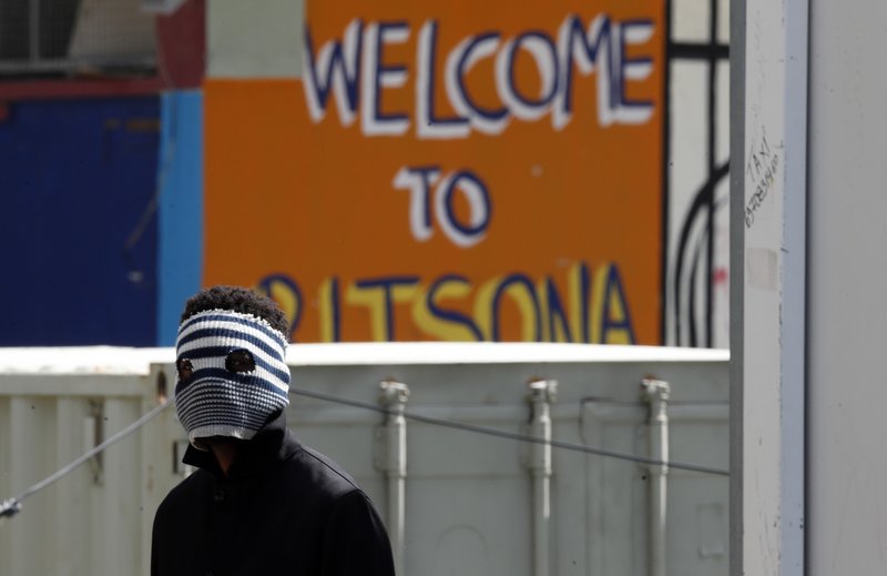 A young migrant covering his face to protect from the new coronavirus stands at the entrance of the Ritsona refugee camp about 80 kilometers (50 miles) north of Athens on Thursday, April 2, 2020. Greek authorities have placed the refugee camp under 14 days quarantine after 20 of its residents tested positive for the COVID-19. During this period nobody would be allowed in or out of the facility. (AP Photo/Thanassis Stavrakis)