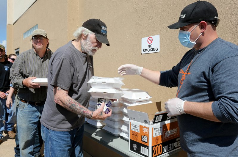 Scott Murr (from right), a volunteer at Genesis Church, helps Jerry Rommel pick up two hot meals Thursday for him and a friend at the Fayetteville church. Genesis provides about 80 people a day with grab-and-go lunches as a way to continue to serve people experiencing homelessness amid the covid-19 pandemic. Meals are served at the church from 11:30 a.m. to 12:30 p.m. Tuesday, Thursday, Friday and Saturday. Go to nwaonline.com/200403Daily/ and nwadg.com/photos for a photo gallery. (NWA Democrat-Gazette/David Gottschalk)