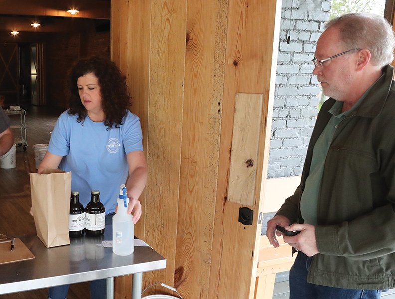 Mary Bradley (left), co-owner of Crystal Ridge Distillery in Hot Springs, fills an order of hand sanitizer for customer David Hamilton on Friday, April 3, 2020.
