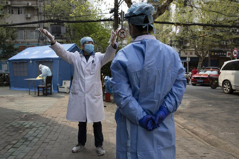 A health worker chats with a colleague Friday in Wuhan in central China’s Hubei province. Sidewalk vendors wearing  face masks got back to business in the city where the coronavirus pandemic began as workers prepared for a national memorial this weekend.
(AP/Ng Han Guan)